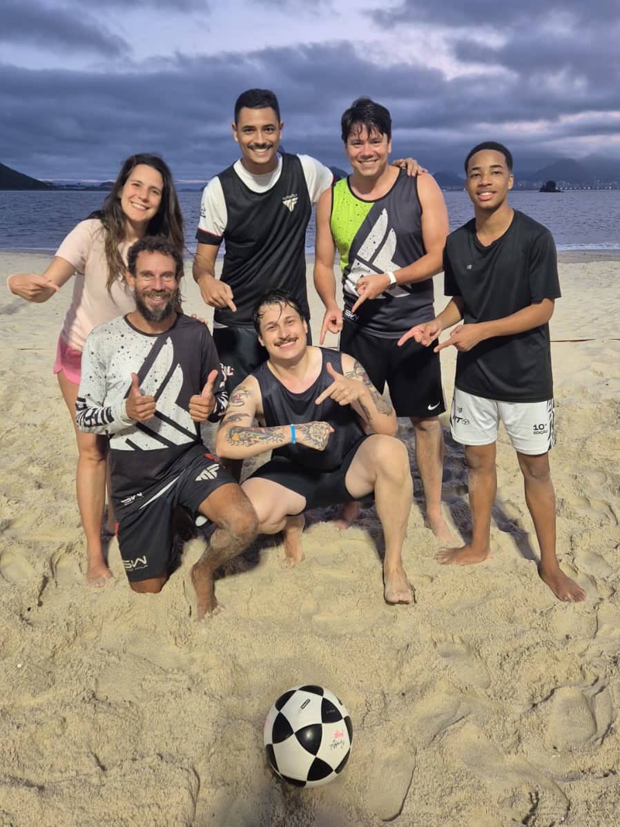 Alunos da MF Futevôlei posando com a bola ao entardecer na praia de Icaraí